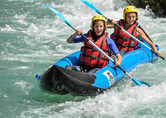 Duo de femmes en canoë-raft bleu naviguant dans les vagues d'une rivière ensoleillée avec Planète Rivière.