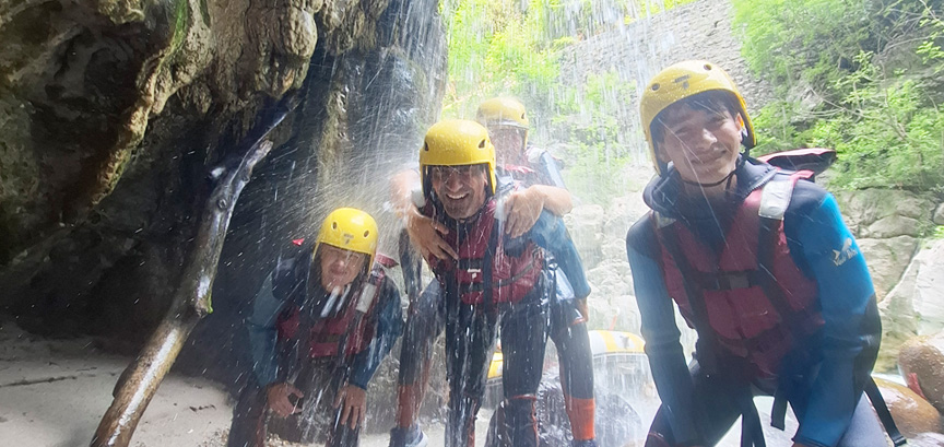 Groupe de sportifs souriants et en famille sous une cascade lors d'un parcours de rafting avec Planète Rivière.