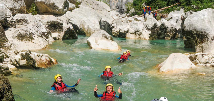 Participants souriants en randonnée aquatique flottant dans une rivière aux eaux turquoise entre les rochers, encadrés par Planète Rivière.