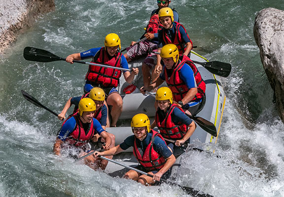 Équipe de sportifs pagayant ensemble sur un radeau pneumatique dans les eaux vives d'une rivière.