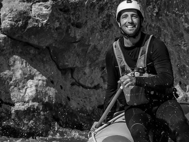 Guide professionnel pratiquant le rafting ou le kayak de rivière, tenant une pagaie, devant une paroi rocheuse.