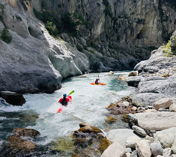 Deux kayakistes naviguant dans un canyon étroit aux parois rocheuses escarpées sur une rivière mouvementée.