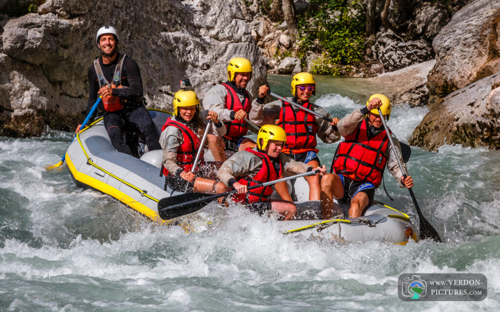 Groupe de rafting souriant naviguant dans des rapides entre des parois rocheuses.