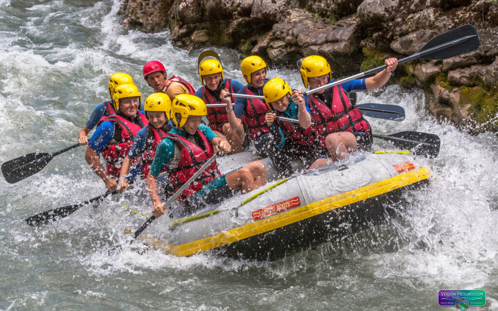 Groupe de personnes en rafting franchissant des rapides tumultueux avec des éclaboussures d'eau.