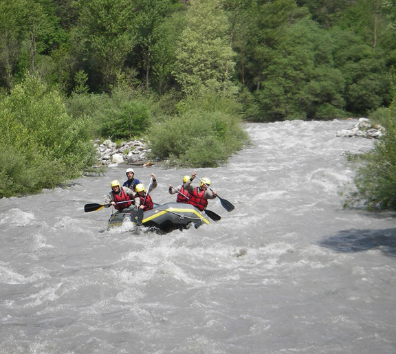 Équipe de rafting en plein effort dans les rapides d'une rivière tumultueuse bordée d'arbres.