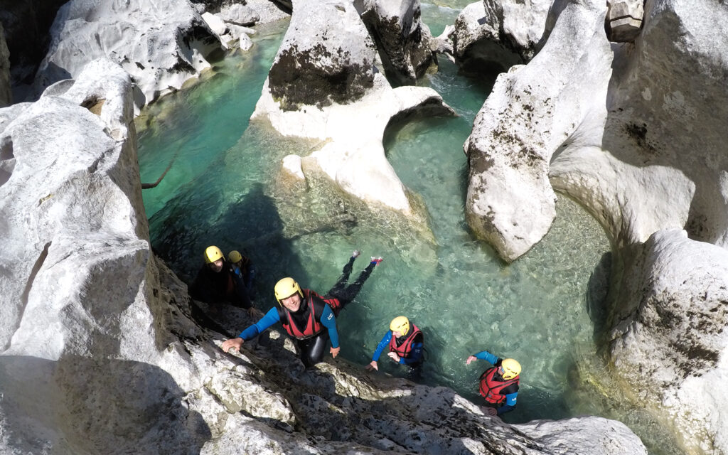 Groupe de personnes pratiquant le canyoning dans une rivière turquoise entourée de rochers blancs sculptés.